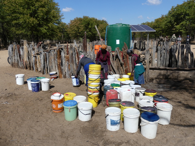 Three villagers in Zimbabwe fill water at a solar-powered well installed by donations from visitors.