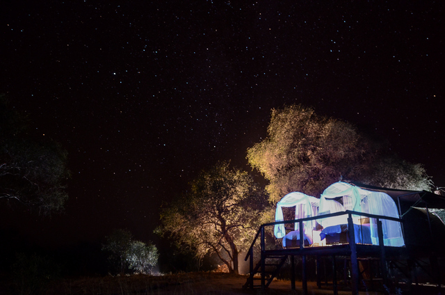 A night shot of tents at Jozibanini Camp in Hwange National Park, with beds set out on a deck so guests can sleep out under the stars