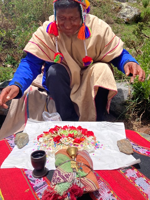 Andean priest praying over a colorful bundle of offerings to the gods presented on a beautiful, red, hand-woven blanket