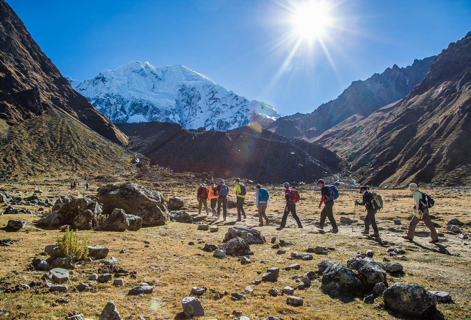 A small group of hikers heading toward the snowy Salkantay Peak on a beautiful, sunny day