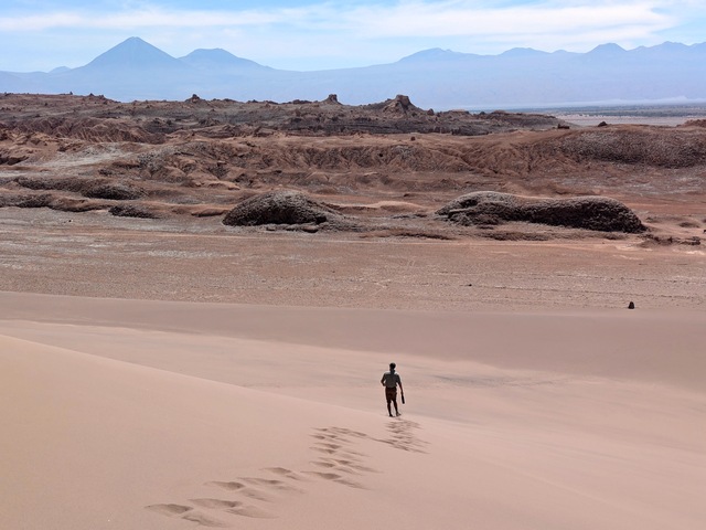 hiker on sand dune with volcano in distance