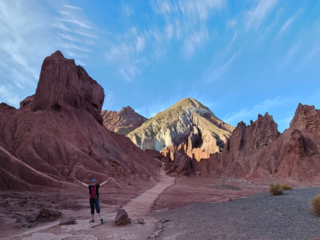 a hiker with her arms out against a red rocky landscape in the Rainbow Valley Atacama Desert