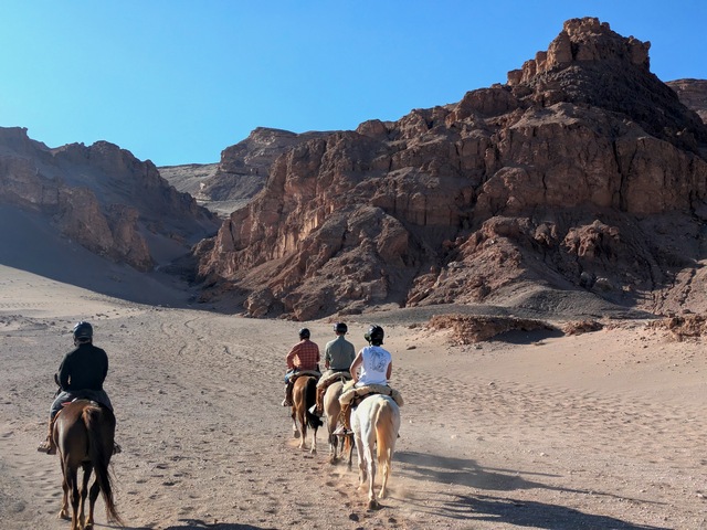 four riders on horseback surrounded by rocky outcrops and sand dunes in the Atacama