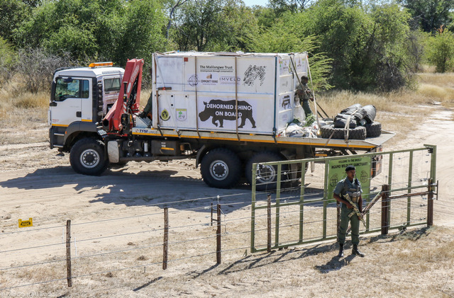 A truck with a logo that reads "dehorned rhino on board" next to a gate with an armed ranger