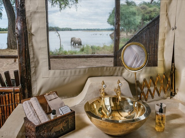 An elephant in the water outside the window of a gold-accented bathroom at Old Mondoro Camp, a luxury safari camp in the Lower Zambezi, Zambia