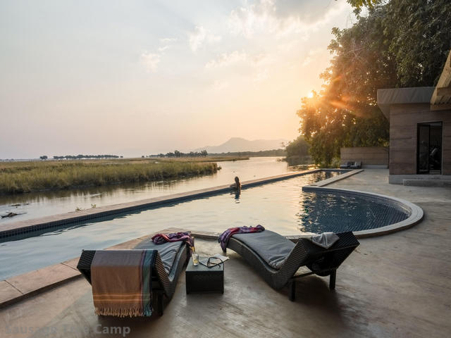 A woman standing at the edge of an infinity pool overlooking the Zambezi River at sunset at Sausage Tree, a luxury safari camp in the Lower Zambezi, Zambia