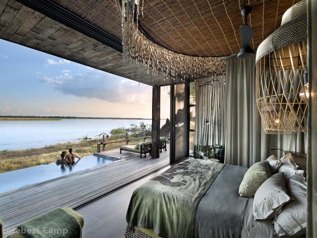 Looking out from a luxurious safari tent at a couple in an infinity pool overlooking the Zambezi River at Lolebezi Camp in the Lower Zambezi National Park, Zambia