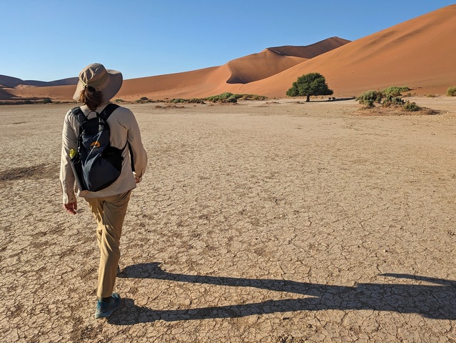 A woman hikes across a flat pan toward Big Daddy Dune at Sossusvlei, Namibia during a luxury safari outing from Camp Sossus