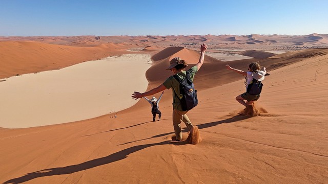 Three hikers gleefully run down Big Daddy Dune at Sossusvlei, Namibia during a luxury safari outing from Camp Sossus
