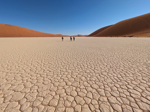Three hikers cross a flat pan toward Deadvlei at Sossusvlei, Namibia during a luxury safari outing from Camp Sossus