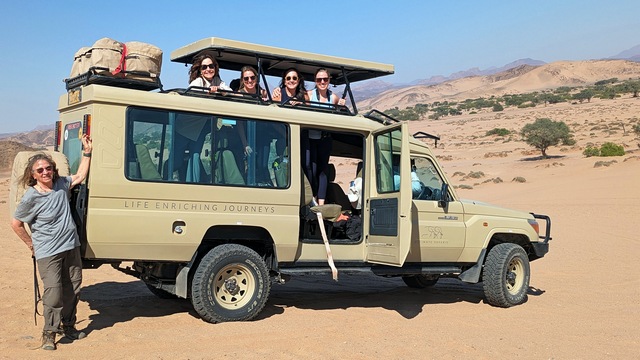A smiling group of guests peering out of their open-top safari vehicle on a luxury safari with Ultimate Namibia Safaris