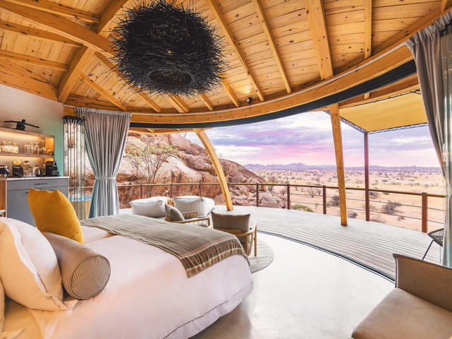 looking across the bedroom out to the rocky desert beyond during a purple and pink sunrise at Onduli Ridge, a luxury safari camp in Damaraland, Namibia