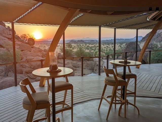 looking across the dining room to the setting sun and desert landscapes outsideduring a beautiful sunset at Onduli Ridge, a luxury safari camp in Damaraland, Namibia