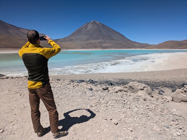 A hiker photographing the emerald waters of Lago Verde in Eduardo Avaroa Reserve