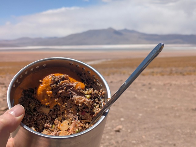 a bowl of quinoa and meat against the mountainous desert landscape of Eduardo Avaroa Reserve