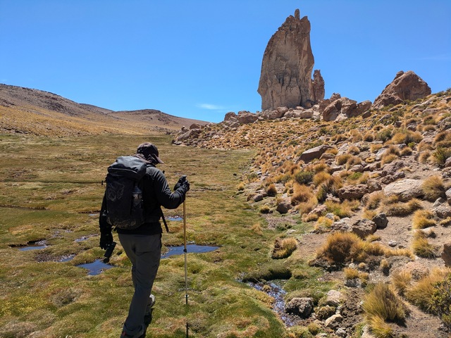 A guide wearing a backpack hikes toward a sandstone rock outcrop in Bolivia
