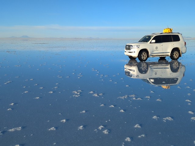 A white vehicle parked on reflective blue waters studded with salt crystals near Explora Uyuni Lodge