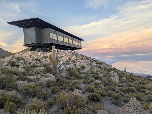 Explora Uyuni Lodge, a small, rectangular building perched on a rocky hilltop overlooking the Uyuni Salt Flats