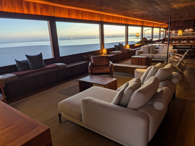 Common area inside Explora Uyuni lodge, with white couches looking out huge poicture windows overlooking the uyuni salt flats at sunset