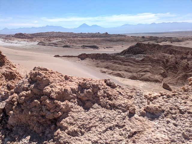 A vast, rocky red landscape of rock formations, salt deposits, and dunes in the Salt Valley of the Atacama
