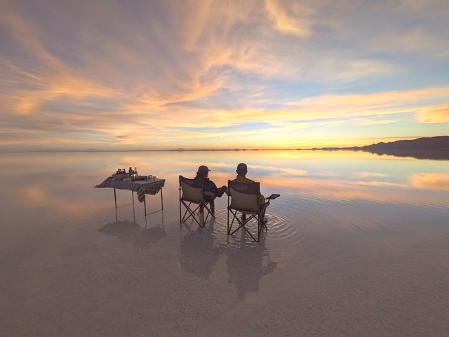 a couple sitting in chairs next to a table enjoying the mirror effect on the uyuni salt flats at sunset