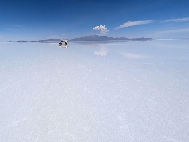 a jeep in the far distance on the uyuni salt flats with the tunupa volcano behind it