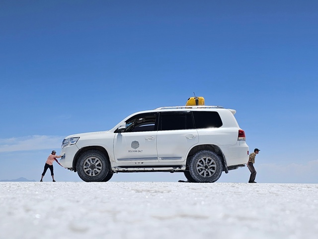 a perspective photo from uyuni salt flats with two tiny people pushing a giant car