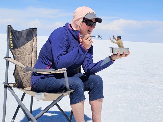 perspective photo from the uyuni salt flats of a woman in a chair eating a tiny man in a can