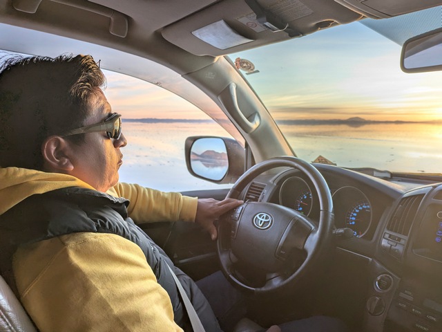 a man inside a vehicle driving across the uyuni salt flats at sunrise