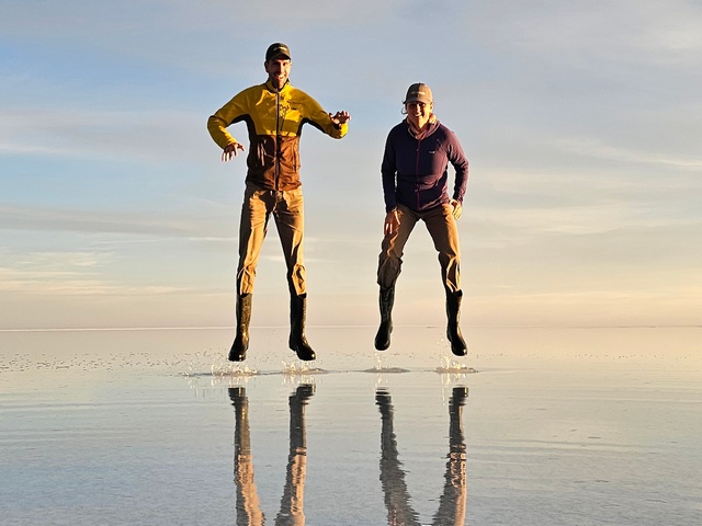 two people in a mid-air jump, with their reflection on the water below them, on the uyuni salt flats