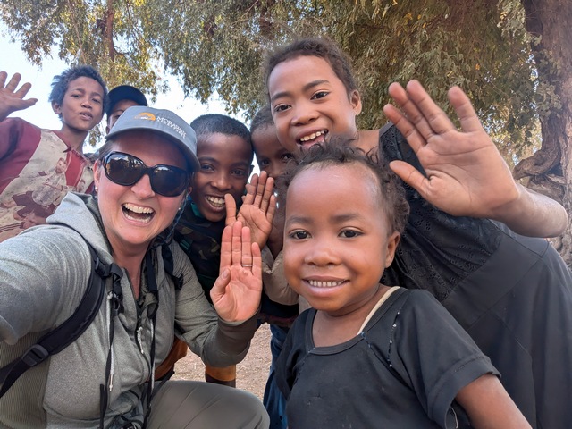 an american tourist and several children in Madagascar smiling and waving at the camera