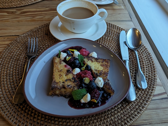 dining table set for breakfast, with a cup of cappucino and a plate of french toast piled with fresh fruit