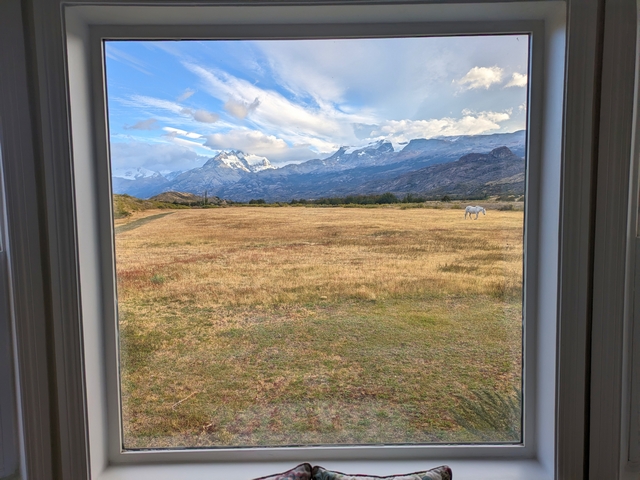 looking out a large picture window to see a lone horse on the steppe of estancia cristina, with large glaciated mountains in the distance