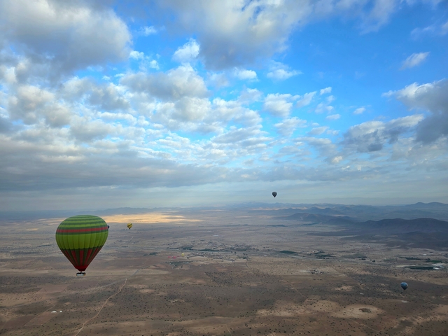 several hot air balloons seen from eye-level up in the clouds drifting over Marrakesh