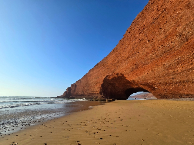 a red stone arch on a sandy beach next to the ocean at Legzira Beach Morocco