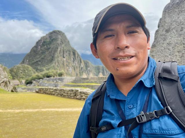 a Peruvian man who guides tours at Machu Picchu smiling, with the ruins of Machu Pichhu visible behind him