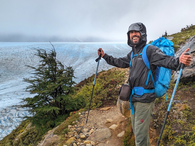 a hiking guide smiles with his arms out in front of the gray glacier in torres del paine patagonia