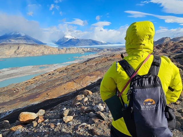 a hiker looks out at the receding toe of the upsala glacier near estancia cristina, with beautiful clouds and colorful rocks
