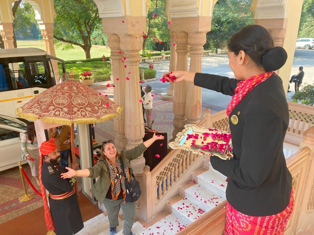 an indian woman throws rose petals at the smiling face of a tourist as she is greeted at a luxury hotel in Jaipur