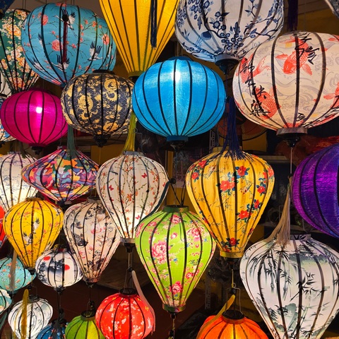 Night view of illuminated traditional lanterns in Hoi An, Vietnam, displayed in a shop with vibrant colors, patterns, and shapes typical of Hoi An Ancient Town.