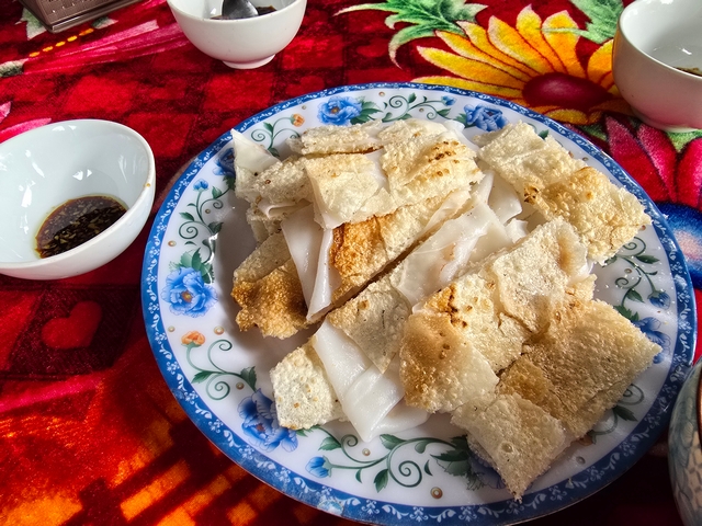 Close-up of toasted rice crackers served on a white porcelain plate with blue floral design, set on a red patterned tablecloth in Hoi An, Vietnam.