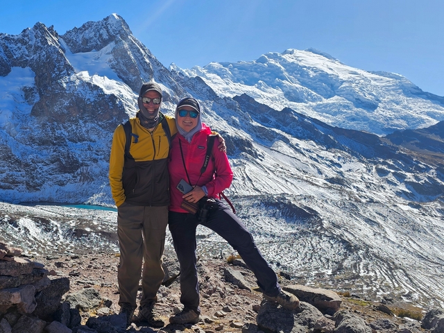 Two smiling trekkers standing with the huge, glaciated Apu Ausangate behind them on a crystal clear day in the high Andes of Peru.