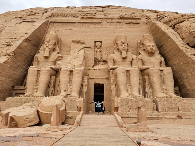 A lone traveler dwarfed next to the 4 giant stone statues of Ramesses II at the Great Temple of Abu Simbel, Egypt.