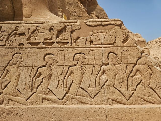 Stone relief carving on the base of the Great Temple of Abu Simbel, Egypt, showing a line of 5 prisoners tied down being dominated by Pharaoh ramesses II.