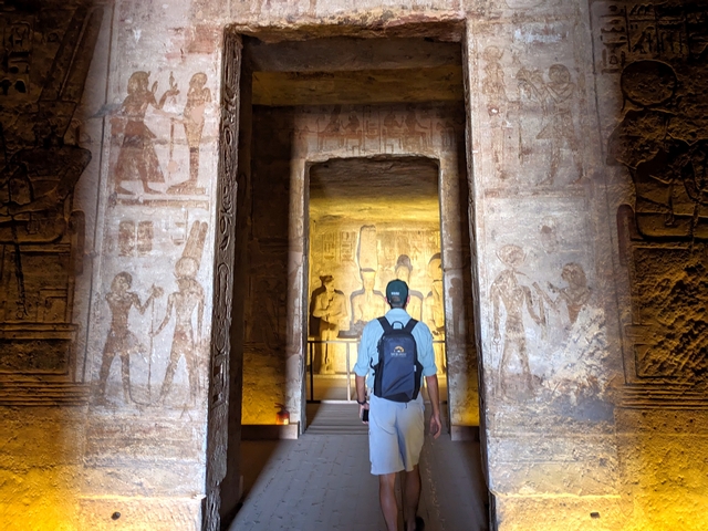 A visitor walks through a stone doorway adorned with images of Ramesses II and the gods inside the Great Temple of Abu Simbel, Egypt.