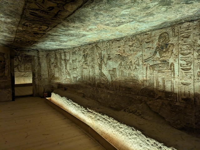 Wall carvings inside a small room at the Temple of Abu Simbel in Egypt, showing images of the Pharaoh Ramesses II and a long, stone bench used to store ceremonial objects.