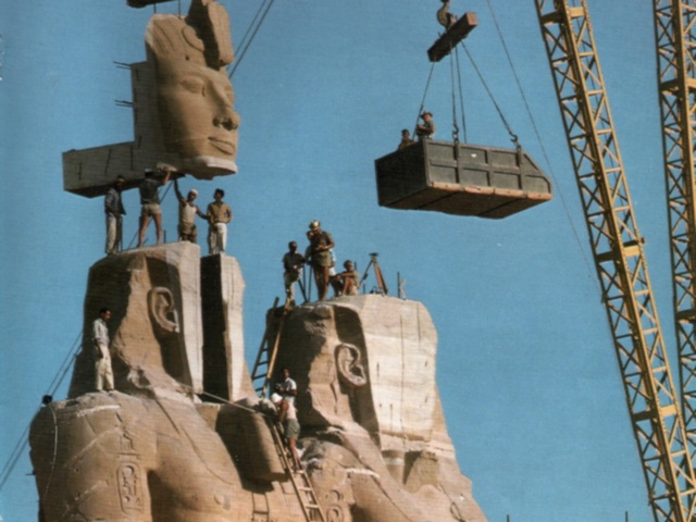 Work men stand atop two giant statues of Ramesses II as a crane lowers the giant carved stone into place during the relocation of the temples in 1967.
