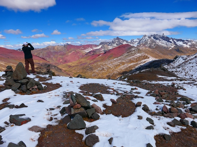 A hiker gazes out at the colorful landscapes near Rainbow Mountain, from the snow-covered slopes of Palomani Pass.