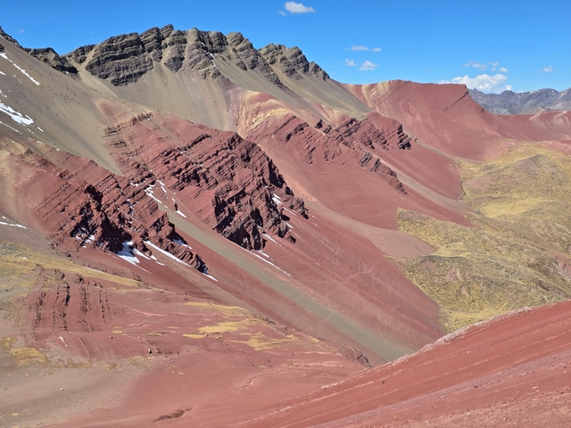 A jagged rocky peak with visible striped of sedimentary layers and rich red colored slopes in the Red Valley near Peru's Rainbow Mountain.