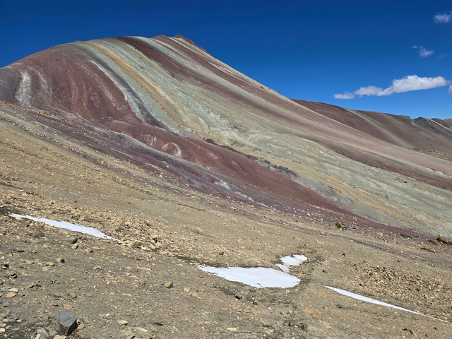 Distant shot of Peru's Rainbow Mountain, showing stripes of rich colors of red, ochre, green, yellow, and purple.
